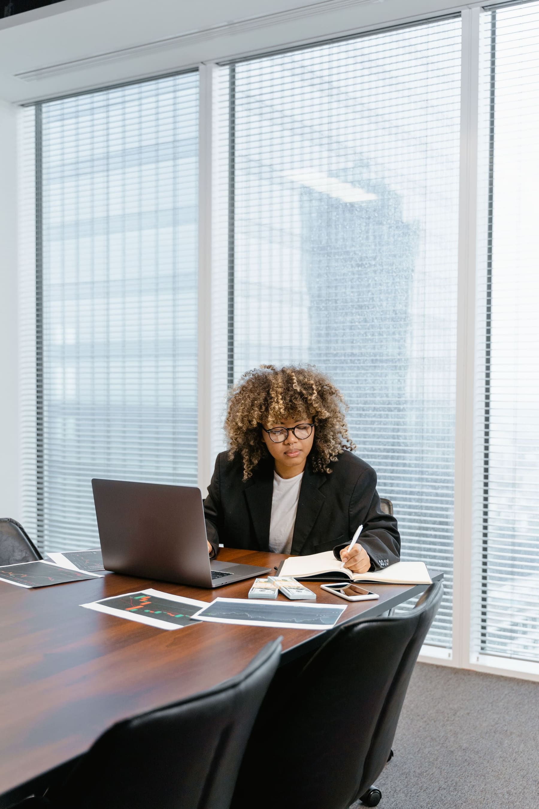 A consultant writing in a notebook beside her laptop and financial charts